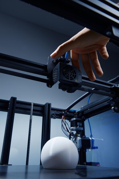 Neutralna pod względem płci ręka modyfikująca ustawienia w drukarce 3D w celu dokończenia drukowania okrągłego białego przedmiotu z przetworzonego plastiku Futurystyczna koncepcja nowych możliwości pracy dla małych firm dzięki drukowi 3D