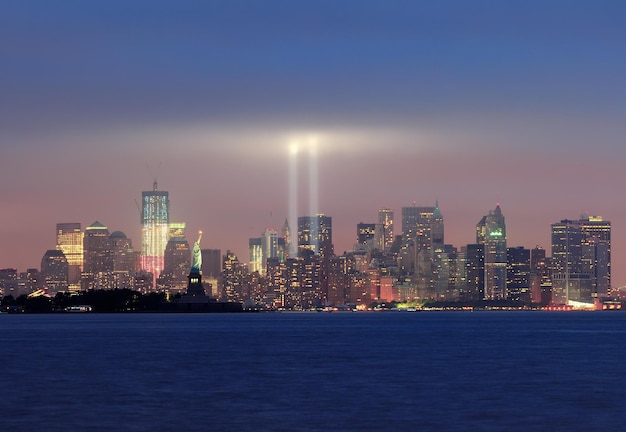 New York City Manhattan panorama śródmieścia w nocy z Statuą Wolności i wiązkami światła na pamiątkę 11 września, patrząc od nabrzeża New Jersey.