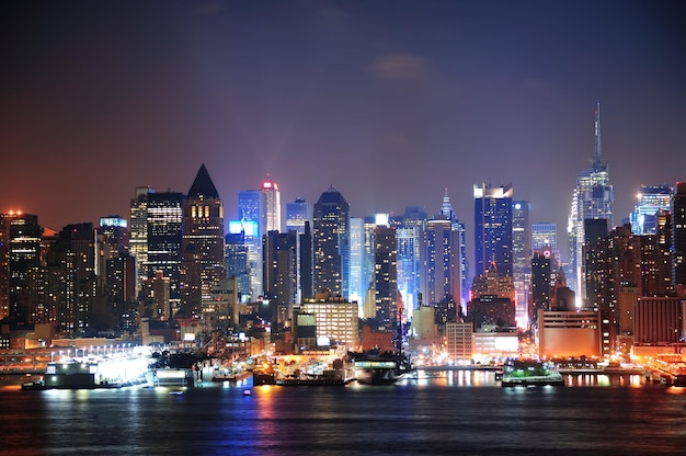 New York City Manhattan skyline w nocy z oświetlonymi drapaczami chmur nad rzeką Hudson z odbiciami.