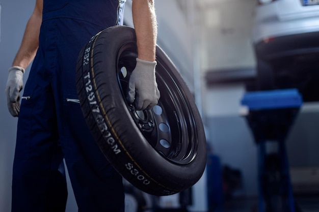 Nie do poznania mechanik samochodowy trzymający oponę samochodową w warsztacie