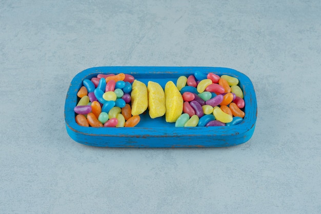 Niebieska drewniana deska cukierków do żucia w kształcie banana z kolorowymi cukierkami z fasoli