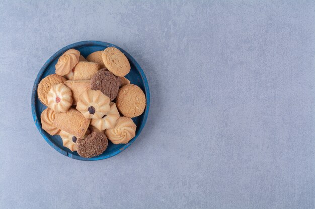Niebieska drewniana tablica ze słodkimi okrągłymi pysznymi ciasteczkami na worze.