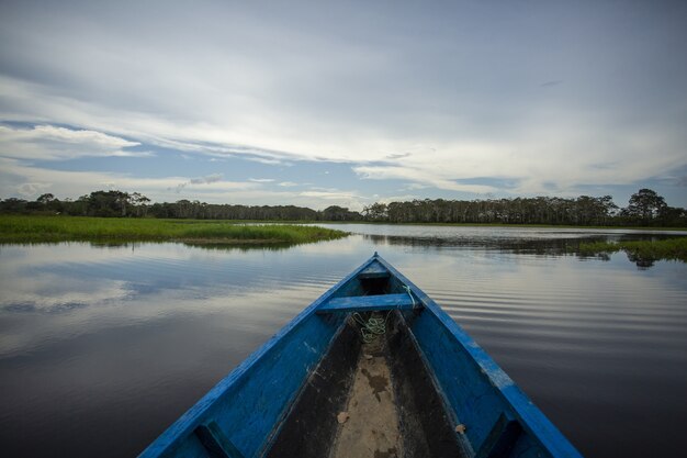 Niebieska drewniana zardzewiała łódź w jeziorze otoczona pięknymi zielonymi drzewami