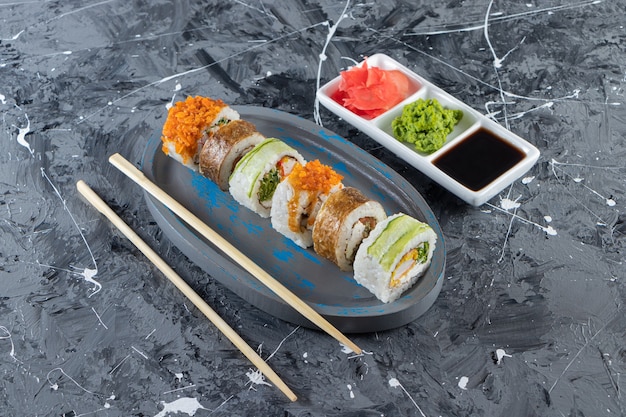 Niebieska płyta różnych sushi rolkach na tle marmuru.
