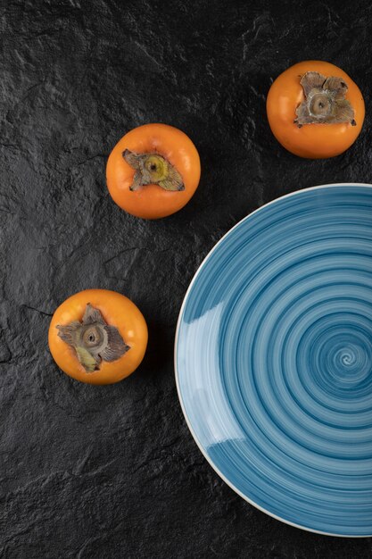Niebieski talerz pysznych dojrzałych persimmons fuyu na czarnej powierzchni