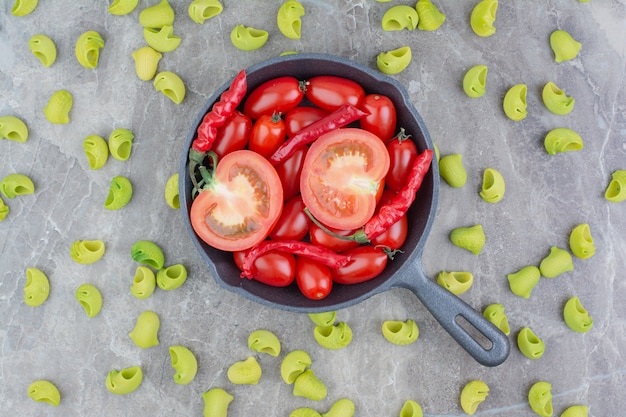 Bezpłatne zdjęcie niegotowane makarony z pomidorkami koktajlowymi i chilli na czarnej patelni
