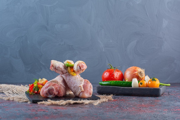 Niegotowane podudzia z kurczaka na czarnej desce do krojenia z warzywami