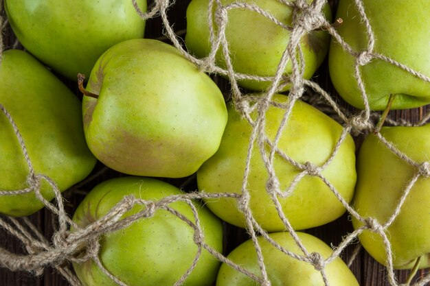 Bezpłatne zdjęcie niektóre zieleni jabłka w netto torbie na drewnianym tle, odgórny widok.