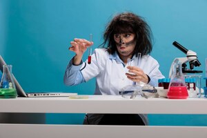 Niemądry, szalony chemik siedzący przy biurku w laboratorium i eksperymentujący z nowymi związkami chemicznymi po wybuchu w laboratorium. specjalista biochemii maniaka z brudnymi substancjami do testowania twarzy.