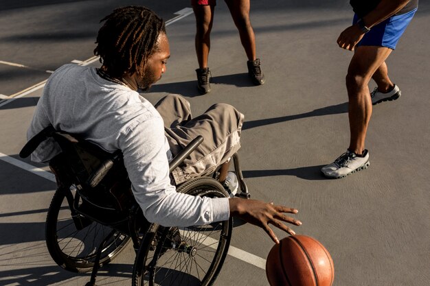 Niepełnosprawny mężczyzna na wózku inwalidzkim grający w koszykówkę z przyjaciółmi na świeżym powietrzu