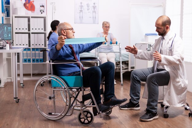 Niepełnosprawny starszy mężczyzna robi swoje ćwiczenia w szpitalu z lekarzem
