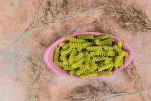 Bezpłatne zdjęcie nieprzygotowany zielony makaron spirali na różowej misce. wysokiej jakości zdjęcie