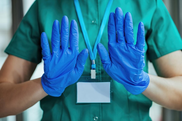 Nierozpoznawalna pielęgniarka w rękawiczkach ochronnych gestykulująca rękoma znakiem stop