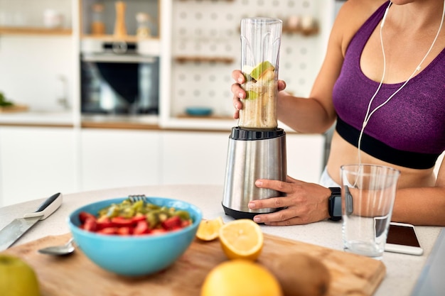 Nierozpoznawalna wysportowana kobieta używająca blendera i przygotowująca smoothie w kuchni