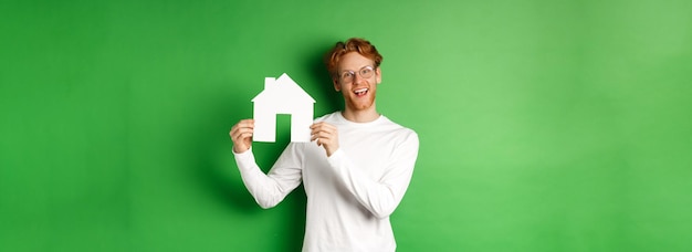 Bezpłatne zdjęcie nieruchomości i kupowanie koncepcji nieruchomości przystojny młody człowiek z rudymi włosami przedstawiający wyszukiwanie wycinanki domu