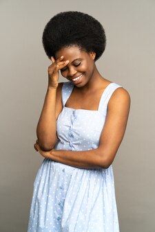 Nieśmiała afroamerykanka z fryzurą afro wygląda na zakłopotaną, uśmiecha się, czuje się bardzo zdezorientowana
