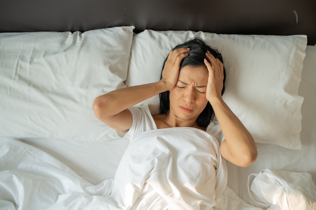 Nieszczęśliwa wyczerpana dojrzała kobieta z zamkniętymi oczami leżąca w łóżku, dotykająca z bliska skroni, zmęczona kobieta cierpiąca na bóle głowy lub migreny, złe samopoczucie, bezsenność, brak snu