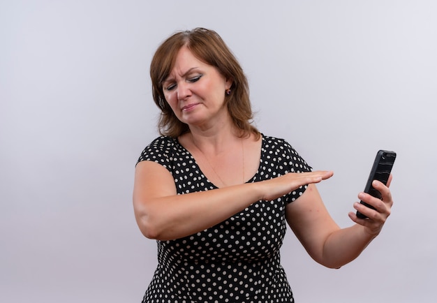 Niezadowolona Kobieta W średnim Wieku, Trzymając Telefon Komórkowy I Wskazując Ręką Na Niego Na Odosobnionym Białym Tle