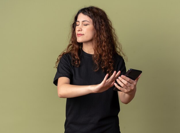 Niezadowolona młoda ładna kobieta trzymająca telefon komórkowy robi gest odmowy z zamkniętymi oczami