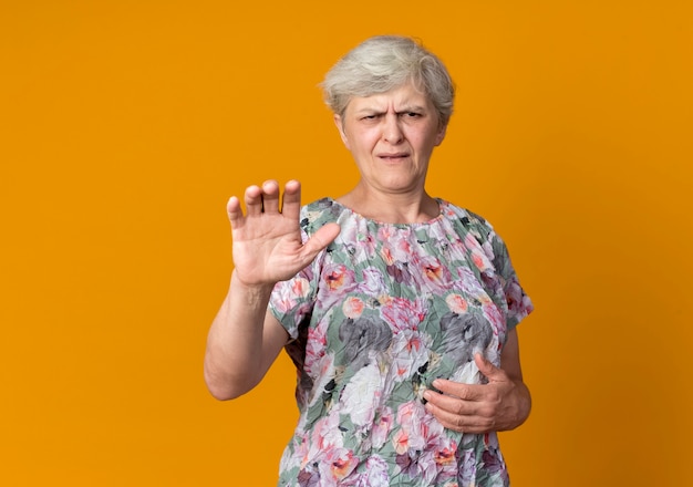 Niezadowolona starsza kobieta podnosi rękę na pomarańczowej ścianie