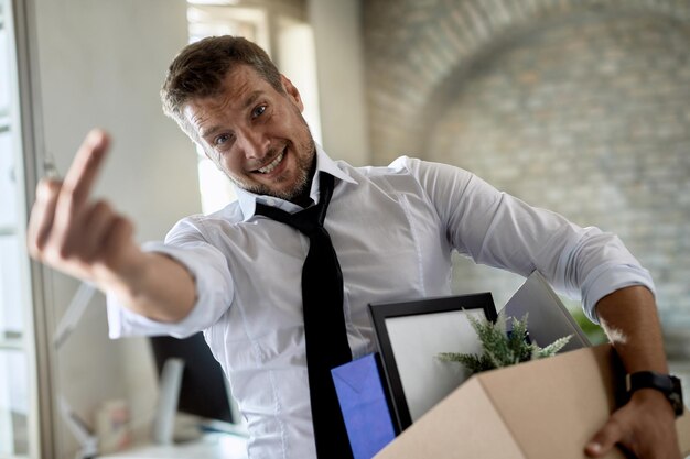 Niezadowolony biznesmen pokazujący środkowy palec w kierunku kamery po utracie pracy w biurze