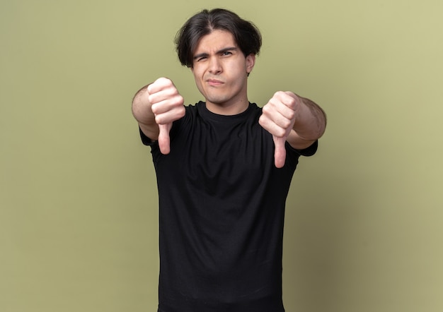 Niezadowolony młody przystojny facet ubrany w czarną koszulkę pokazujący kciuki w dół, odizolowany na oliwkowozielonej ścianie
