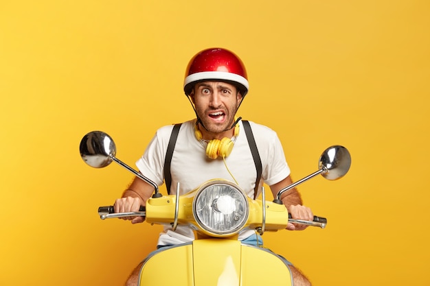 Bezpłatne zdjęcie niezadowolony przystojny mężczyzna kierowca na skuterze z czerwonym kaskiem