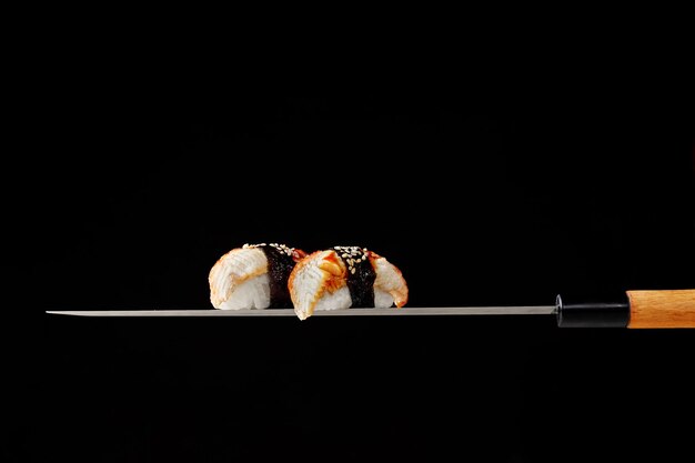 Nigiri sushi z węgorzem podawane na ostrzu tradycyjnego japońskiego noża na czarnym tle