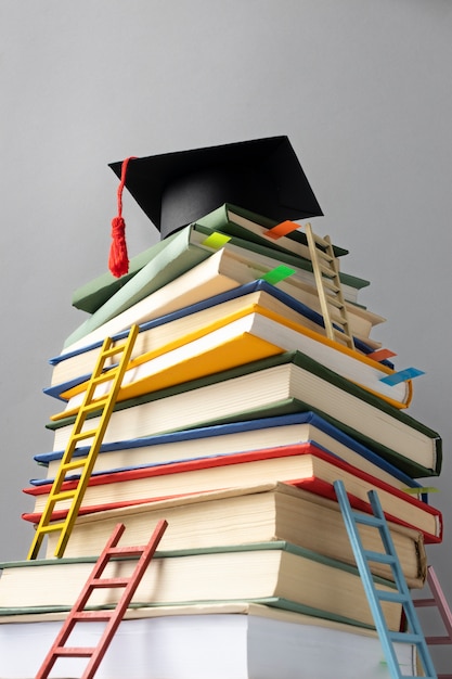 Bezpłatne zdjęcie niski kąt ułożonych w stos książek, czapka maturalna i drabiny na dzień edukacji
