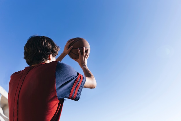 Niskiego kąta widok nastoletniego chłopaka mienia koszykówka przeciw niebieskiemu niebu