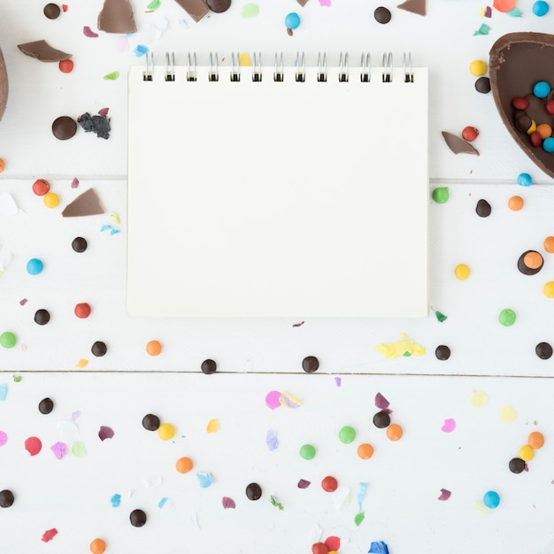 Bezpłatne zdjęcie notatnik między cukierkami, czekoladowym jajkiem i confetti
