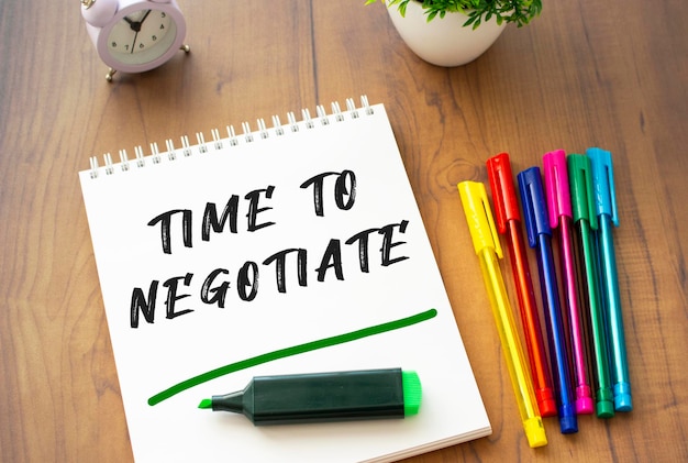 Notatnik na sprężynie z napisem czas do negocjacji leży na brązowym drewnianym stole.