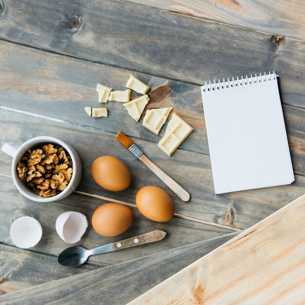 Bezpłatne zdjęcie notatnik w pobliżu kawałków czekolady; jajka i orzechy włoskie na powierzchni drewnianych