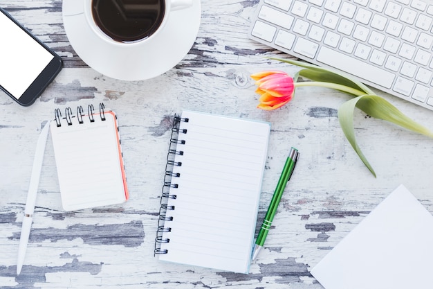 Bezpłatne zdjęcie notatniki i filiżanka kawy blisko smartphone i klawiatury na biurku z tulipanowym kwiatem