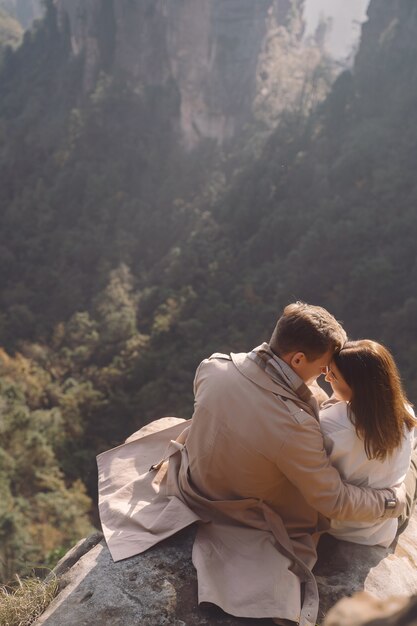 Nowo zakochana para ściska i trzyma się za ręce, gdy siedzą na skale w parku narodowym Zhangjiajie