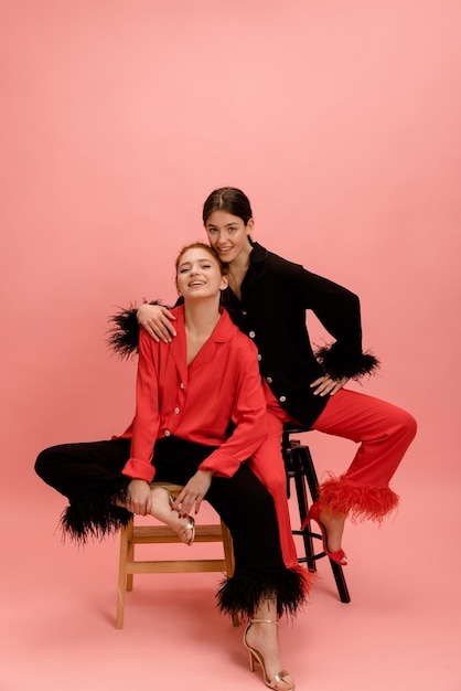 Nowoczesne kaukaskie panie w wieku 20 lat noszą koszule i spodnie pozują siedząc w studio na różowym tle Eleganckie trendy w modzie