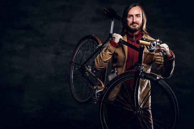 Bezpłatne zdjęcie nowoczesny brodaty hipster w czerwonym swetrze trzyma rower podczas pozowania dla fotografa.