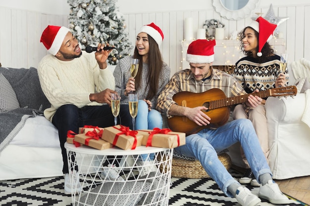 Noworoczne karaoke. wieloetniczna firma grająca na gitarze i śpiewająca świąteczną piosenkę w domu, kopia przestrzeń