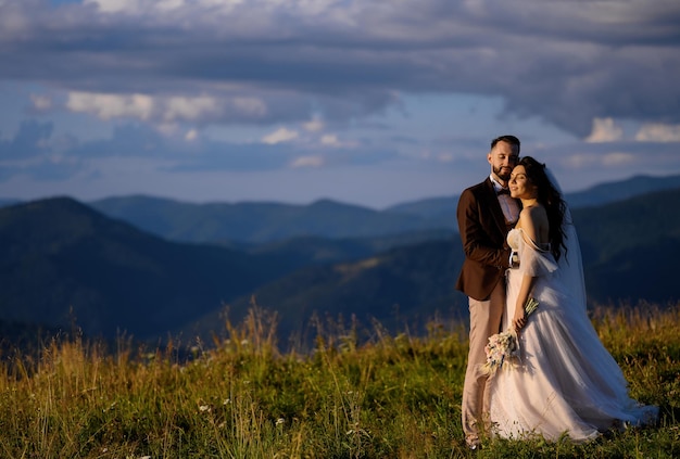 Bezpłatne zdjęcie nowożeńcy patrzący na zachód słońca pozujący na wzgórzu