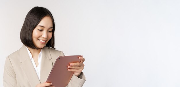Obraz azjatyckiej bizneswoman używającej cyfrowego tabletu, patrzącej na gadżet i uśmiechniętej stojącej na białym tle