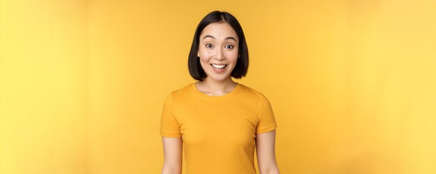 Obraz azjatyckiej dziewczyny wyglądającej na zaskoczoną, reagującej na zdziwione unoszące się brwi, zaimponowane stojąc na żółtym tle