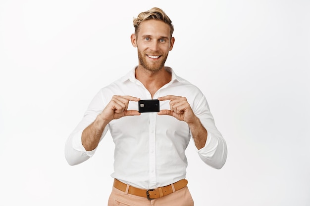 Bezpłatne zdjęcie obraz biznesmena pokazującego kartę kredytową uśmiechniętego i wyglądającego na zadowolonego stojącego na białym tle