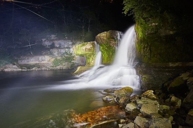 Obraz świecących białych wodospadów z pokrytymi mchem kamieniami w lesie w nocy w cataract falls