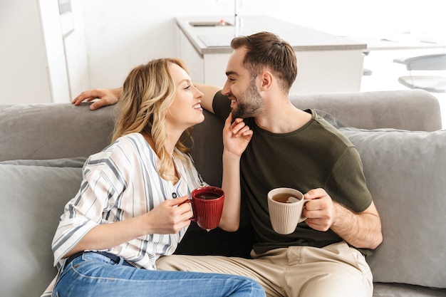 Obraz szczęśliwa młoda para kochających siedzi na kanapie w domu, pijąc herbatę.