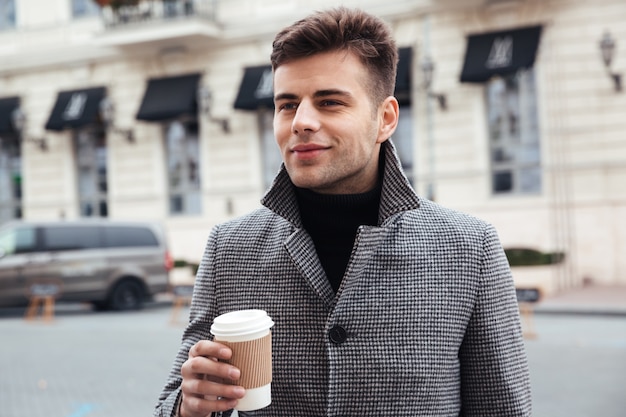 Obrazek cieszy się wynos kawę od papierowej filiżanki przystojny mężczyzna, podczas gdy idący w dół pustą ulicę