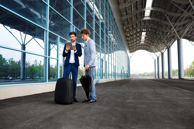 Obrazek dwa młodego biznesmena opowiada na terminal i trzyma pastylkę