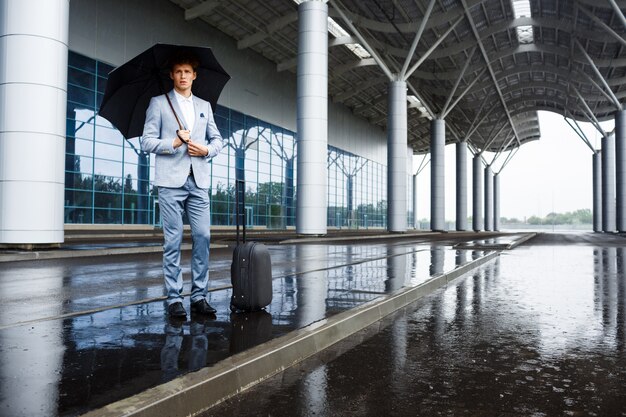 Obrazek ufny młody redhaired biznesmen trzyma czarnego parasol w deszczu przy lotniskiem