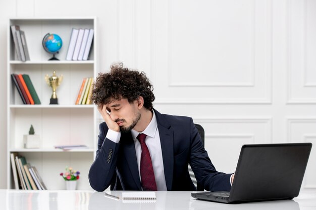 Obsługa klienta kędzierzawy młody mężczyzna w garniturze biurowym i czerwonym krawacie z laptopem zmęczony