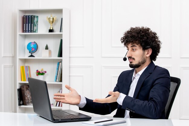 Obsługa klienta przystojny kręcony mężczyzna w garniturze biurowym z komputerem i zestawem słuchawkowym macha rękami