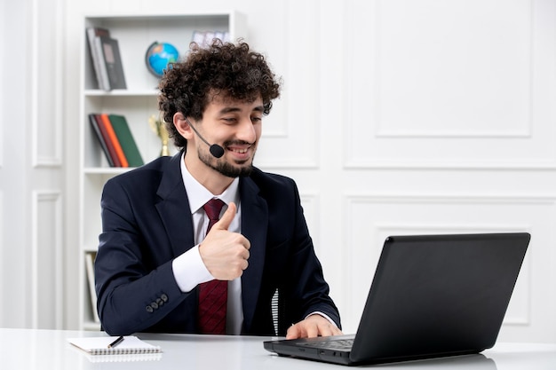 Obsługa klienta przystojny młody facet w garniturze biurowym z laptopem i zestawem słuchawkowym uśmiechający się szczęśliwie